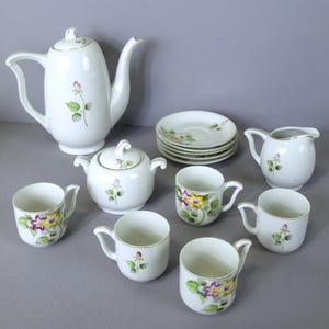 May include: A white porcelain tea set with floral designs. The set includes a teapot, creamer, sugar bowl, six cups, and six saucers.