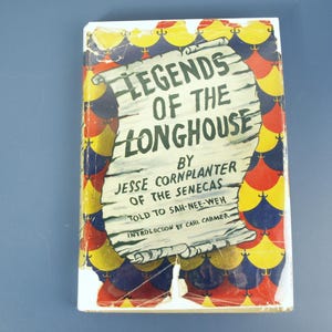 May include: A vintage book titled "Legends of the Longhouse" by Jesse Cornplanter of the Senecas. The cover features a scroll design with text and a colorful pattern of red, yellow, and blue shapes. The book is on a blue surface.