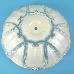 May include: A round, translucent white glass light fixture shade featuring a scalloped, ribbed surface design. The shade is accented with raised, textured blue detailing that follows the contours of the ribs and includes a central circular opening.