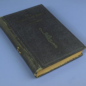 Könnte beinhalten: Ein Vintage-Buch mit dem Titel "My Basketball Bible" von Forrest C. Allen. Der Einband ist dunkelblau mit einer goldenen Illustration eines Basketballspielers und goldener Schrift. Das Buch hat ein abgenutztes Aussehen.