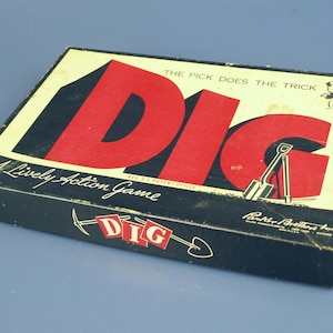 Puede incluir: Caja de juego de mesa vintage "DIG". La caja es negra con una parte superior color crema y letras rojas grandes que deletrean "DIG". La caja también presenta el texto "A Lively Action Game" y una ilustración de una persona con una pala.