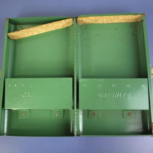 May include: Open, empty green metal tool box with the name "GREENLEE" embossed on the inside. The box has two compartments, each with a hinged shelf. The box is open, revealing the interior.