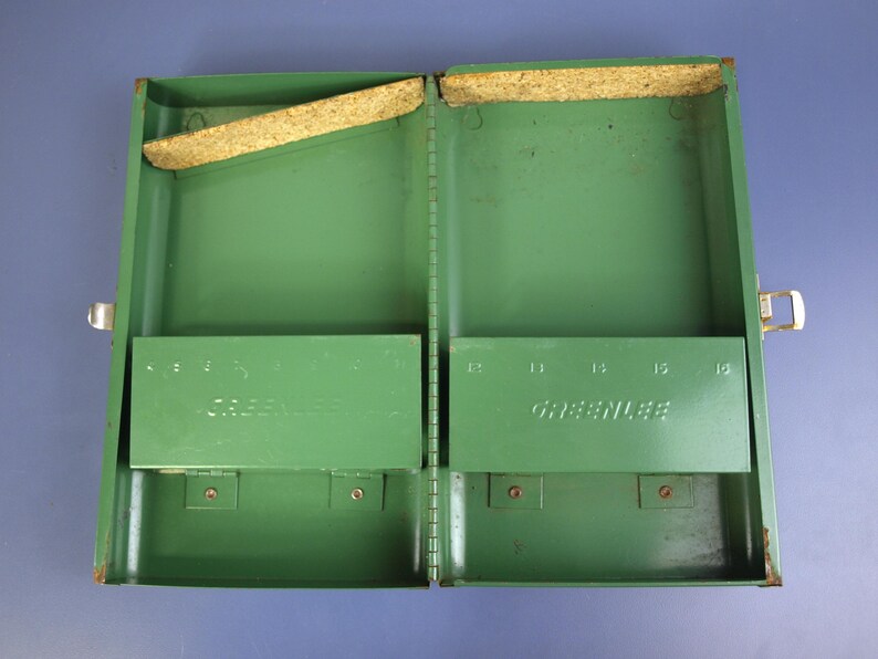 May include: Open, empty green metal tool box with the name "GREENLEE" embossed on the inside. The box has two compartments, each with a hinged shelf. The box is open, revealing the interior.