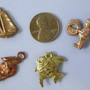 May include: Five gold-toned metal charms: a sailboat, a fish, a rabbit, a drummer, and a US penny. The penny is dated 1960 and has the words "In God We Trust" and "Liberty" on it.