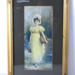 May include: A framed watercolor painting of a young woman in a yellow dress and white bonnet standing in a garden setting. She is holding a basket of flowers and is looking at the viewer.