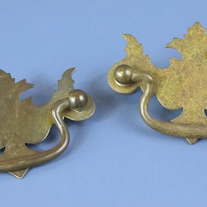 Puede incluir: Dos tiradores de cajón antiguos de latón con un diseño en forma de hoja. Cada tirador presenta un asa curvada y detalles decorativos, ideales para la restauración de muebles antiguos. Los tiradores miden aproximadamente 10 cm de ancho.