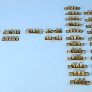 May include: A collection of 30 gold-toned electrical terminal strips with multiple connection points. The strips are arranged in rows on a light blue surface.