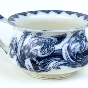 Pode incluir: Bacia de cerâmica branca com um desenho floral azul. A bacia tem uma pega e uma borda larga com um padrão azul. O exterior apresenta um detalhado motivo floral azul e branco.