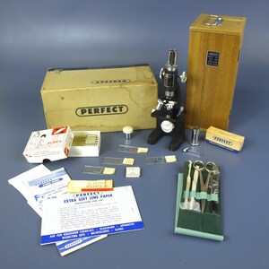 May include: A vintage Perfect brand student microscope set including a black metal microscope, a wooden storage case, a cardboard box, glass slides, a small tool kit with scissors, lens paper, and instructional pamphlets with the Perfect logo.
