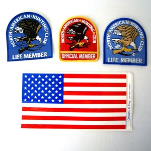 Könnte beinhalten: Drei gestickte Aufnäher in Blau, Rot und Gelb mit dem Text "North American Hunting Club" und den Worten "Life Member" und "Official Member". Ein Aufkleber der amerikanischen Flagge mit dem Text "Official U.S. Flag" befindet sich unter den Aufnähern.