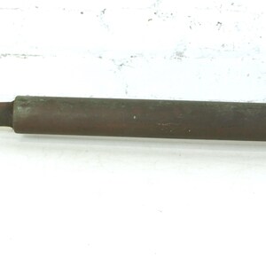 May include: A vintage metal hand pump featuring a long, cylindrical, dark brown rusted body with a smooth, polished brass-colored extension rod and a flat, T-shaped handle at one end, showing signs of age and oxidation throughout the surface.