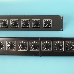 May include: Two black control panels with knobs. The top panel has six knobs, and the bottom panel has twelve knobs. Each knob is black with a white indicator. The panels are rectangular and have mounting holes.