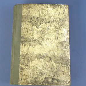 May include: A vintage book with a cover resembling birch bark. The cover has a textured, light beige and gray pattern, with a green spine. The book is closed and appears to be in good condition, suggesting it is well-preserved.