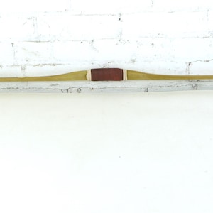 May include: A long, curved bow with a light brown finish. The bow features a dark brown leather grip in the center. The tips of the bow are slightly curved. The bow is set against a white background.