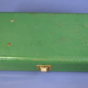 May include: A rectangular, vintage green metal box with a hinged lid and a clasp closure. The box shows signs of wear, with some rust and scratches visible on the surface. The clasp is a gold color.