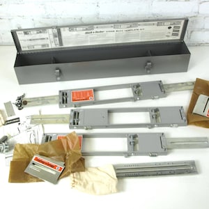 May include: A vintage Black & Decker Junior Miter Template Kit. The image shows a grey metal toolbox with an open lid, templates, and small parts. The kit is displayed on a white surface. The templates are grey.