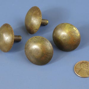 以下が含まれることがあります： 古びた仕上げの真鍮製キャビネットノブ4個。ノブは丸みを帯びた楕円形で、青い面に配置されています。サイズの目安としてペニーが含まれています。