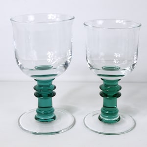May include: Two clear glass wine glasses with green bases. The glasses are different sizes.