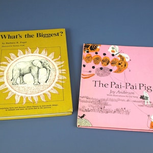 May include: Two vintage children's books. One is yellow with an elephant illustration and the title "What's the Biggest?". The other is pink, titled "The Pai-Pai Pig". Both books are on a blue background.