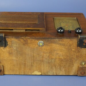 Puede incluir: Una radio vintage de madera con un gabinete de madera marr&oacute;n y una cara negra. La radio tiene dos perillas negras y un dial de vidrio con un fondo dorado.