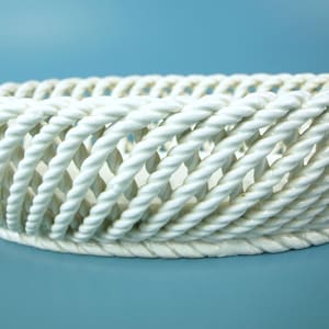 May include: White ceramic basket with a woven rope design. The oval-shaped basket has a wide opening and a textured surface. The basket is set against a light blue background. This decorative piece is suitable for various uses.