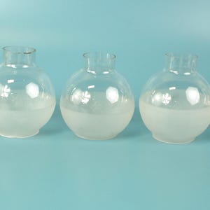 May include: Five clear glass globes arranged in a horizontal row. Each globe features a spherical body with a short, cylindrical neck opening at the top. The lower half of each glass globe has a frosted, opaque white finish, while the top remains clear.