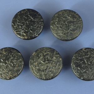May include: Five circular buttons with a dark, textured, and uneven surface finish. Each button features a rugged, mottled appearance with deep indentations and raised areas, creating a consistent, weathered look across all five individual pieces.