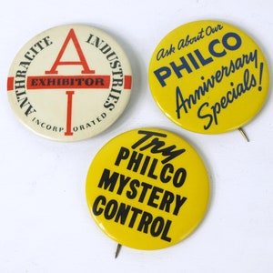 Op de afbeelding: Drie ronde knopen. De eerste knoop is wit met rode en zwarte tekst die "Anthracite Industries Incorporated Exhibitor" luidt. De tweede knoop is geel met blauwe tekst die "Ask About Our Philco Anniversary Specials!" luidt. De derde knoop is geel met zwarte tekst die "Try Philco Mystery Control" luidt.