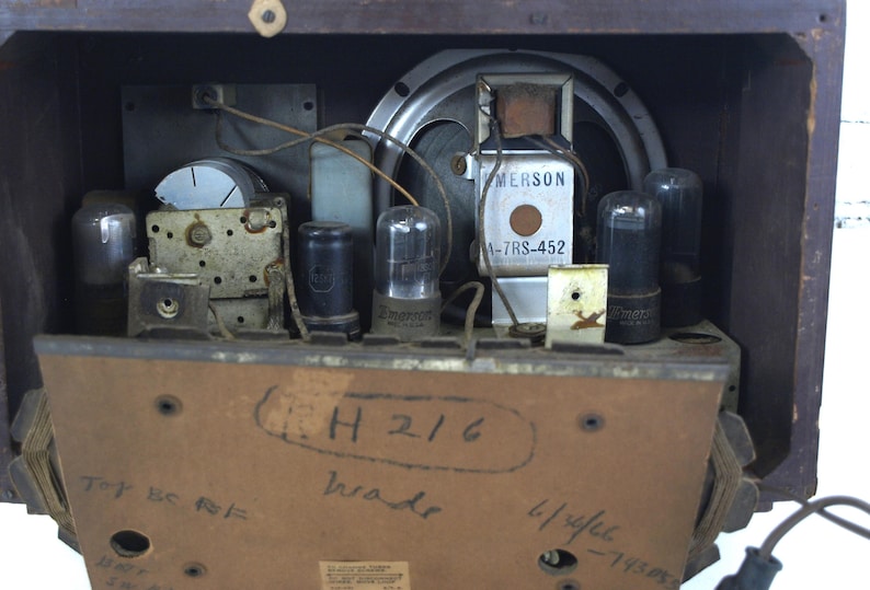 Puede incluir: Vista interior de una radio Emerson vintage con un altavoz, varios tubos de vac&iacute;o y una etiqueta que dice "Emerson A-7RS-452". La radio tiene un gabinete de madera y una etiqueta manuscrita en la parte posterior que dice "(L)H 216 brade 4/reflect - 11588".