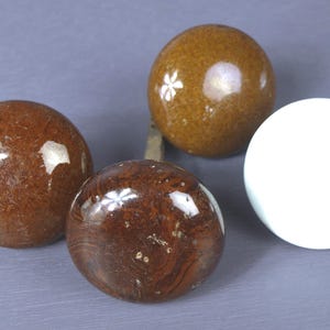 May include: Four spherical cabinet knobs. Three are brown with a floral design, and one is white. The knobs have a glossy finish. They are likely made of ceramic or glass. The knobs are for a cabinet.