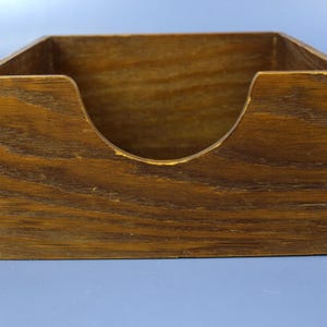 May include: A rectangular wooden box with a dark brown stained finish and visible wood grain. The front panel features a U-shaped cutout for easy access, and the corners are constructed with interlocking finger joints for structural stability.