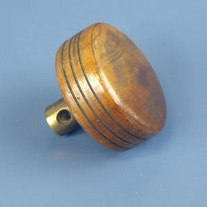 May include: A wooden cabinet knob with a brass base. The knob is oval-shaped with three dark grooves and a warm brown finish. The brass base has a hole for mounting.