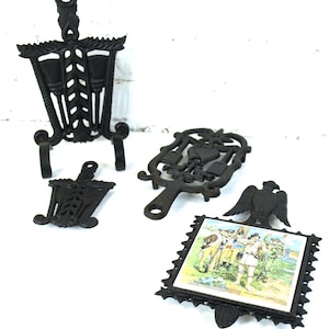 Salvamanteles antiguos de hierro fundido: dos salvamanteles Harner Broom & Wheat de John Zimmerman, pájaros n.° 15 de Distelfink y un inserto de baldosas de cerámica del Ejército Continental (1976-79)