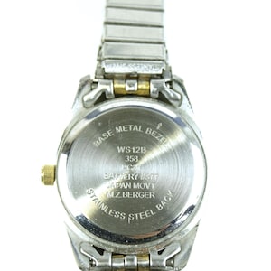 May include: A silver-toned wristwatch with a stainless steel back and a metal bezel. The watch band is made of silver-colored metal links. The watch face has text that reads "WS12B 358" and "JAPAN MOV'T".