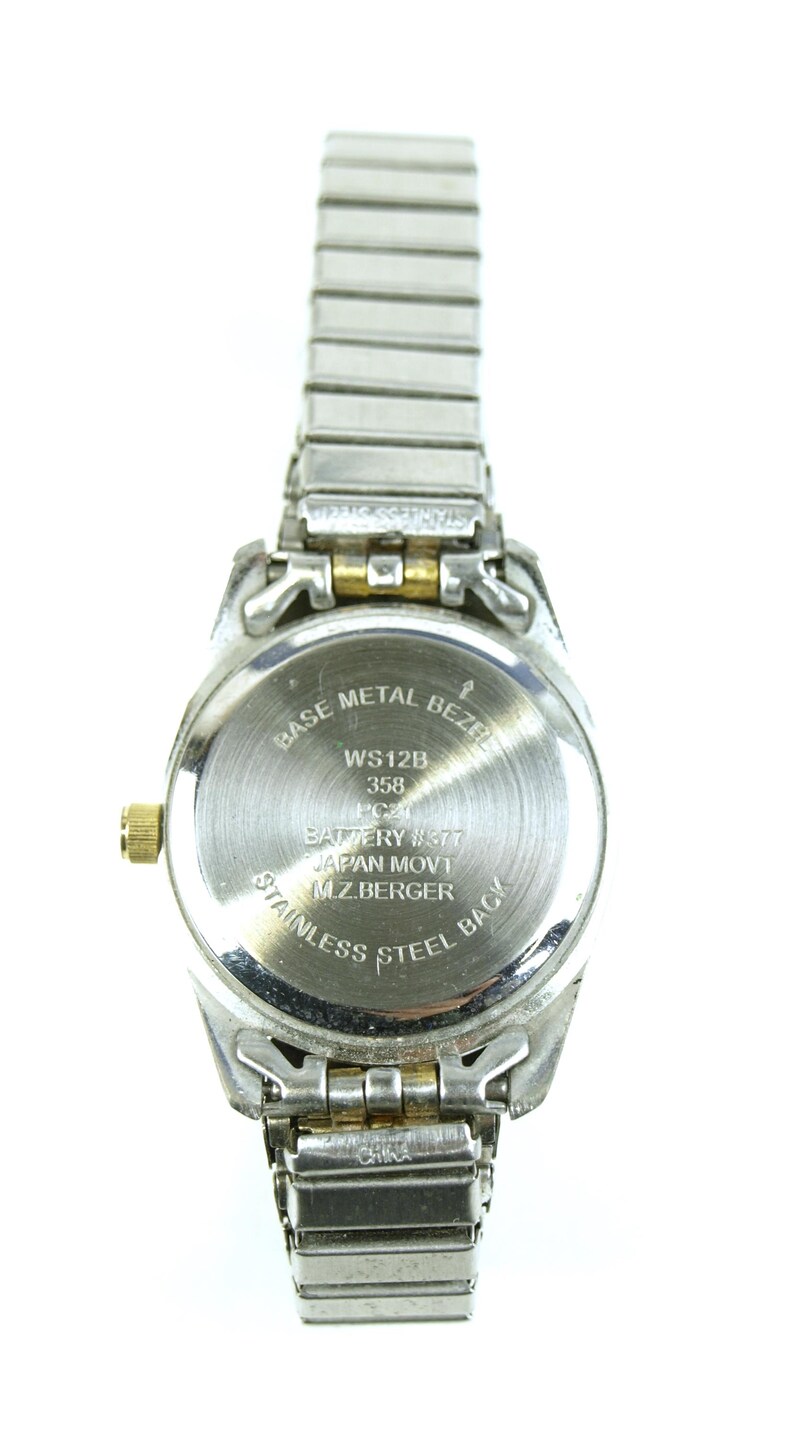 May include: A silver-toned wristwatch with a stainless steel back and a metal bezel. The watch band is made of silver-colored metal links. The watch face has text that reads "WS12B 358" and "JAPAN MOV'T".