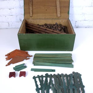 May include: A vintage wooden toy building set in a green wooden box. The set includes various sized wooden pieces in green, brown, and red.