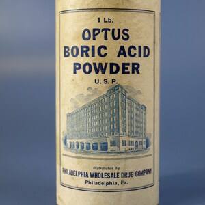 May include: A cylindrical container of Optus Boric Acid Powder, with blue text on a cream background. The label includes the text "1 Lb.", "OPTUS BORIC ACID POWDER", and "U.S.P.". The bottom of the container reads "PHILADELPHIA WHOLESALE DRUG COMPANY".
