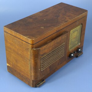 Puede incluir: Una radio vintage de madera con un gabinete de madera marr&oacute;n y una rejilla de altavoz negra. La radio tiene un dial con una cara de vidrio y algunas perillas en la parte delantera.