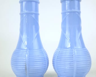 May include: Two light blue glass salt and pepper shakers. The shakers have a ribbed design on the bottom and a decorative pattern on the upper portion. One shaker has a metal lid. A penny is in the foreground.