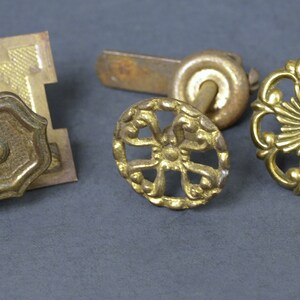 Könnte beinhalten: Vier vergoldete Metall-Schrankknöpfe mit filigranen Designs. Die Knöpfe sind rund und haben verschiedene Muster, darunter ein Blumenmuster, ein geometrisches Muster und ein einfaches, kreisförmiges Muster.