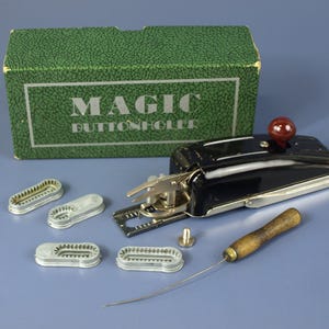 May include: A vintage black and silver Magic Buttonholer sewing machine with a red knob, a wooden handle, and several silver buttonhole templates. The green box has the words "MAGIC BUTTONHOLER" printed on it.