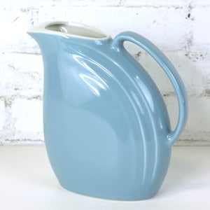 May include: A light blue ceramic jug with a curved handle and a smooth, glossy finish.