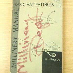 May include: A vintage millinery manual titled "Basic Hat Patterns" by Mrs. Gladys Old. The cover is light green with black text and a pink border. The cover features illustrations of hat-making tools and the word "Millinery" in a cursive font.