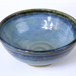 Op de afbeelding: Een blauwe keramische kom met een groene rand. De kom heeft een gespikkeld glazuur en een licht swirl-patroon in de bodem.