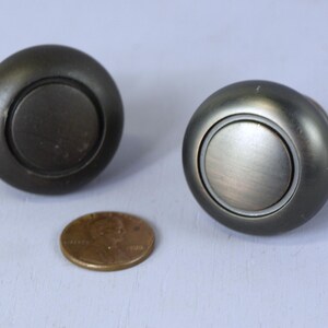 以下が含まれることがあります： 円形の銀色のキャビネットノブ2個。隆起した同心円のデザイン。ノブはブラッシュ仕上げです。