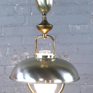 May include: A vintage brass and silver-toned pendant light fitting. The fitting features a domed shade, a decorative brass frame, and an elongated brass body. The light is suspended from a brass canopy and has a decorative glass bulb cover.