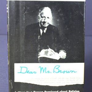 May include: A book cover with a black and white portrait of a man in a suit. The title "Harry Emerson Fosdick" is in red, and "Dear Mr. Brown" is in blue script. The book's title is "Letters to a Person Perplexed about Religion".