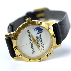 Reloj de pulsera analógico de cuarzo vintage con publicidad financiera de Keystone. Reloj dorado para mujer con correa de cuero negro. Funciona.