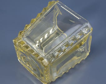 May include: A clear glass jar with a yellow tint and a geometric pattern around the rim.