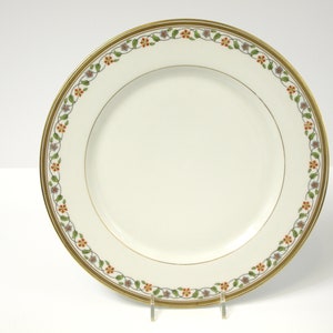 Puede incluir: Un plato de porcelana blanca con borde dorado y un diseño floral en tonos naranja, verde y azul.